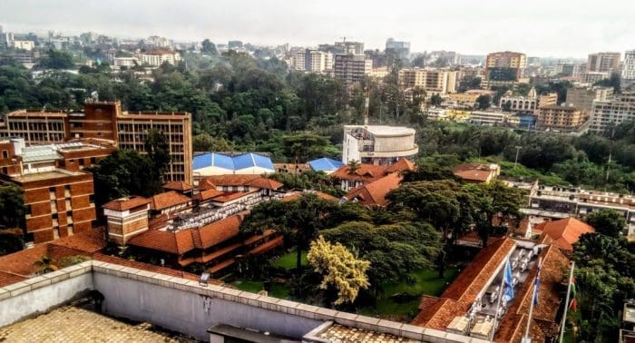 view of a cityscape with a mix of modern and older buildings, green trees, and a cloudy sky